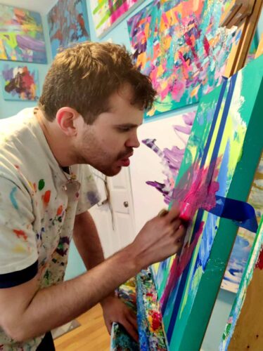 Young man painting with bright colors on a large canvas